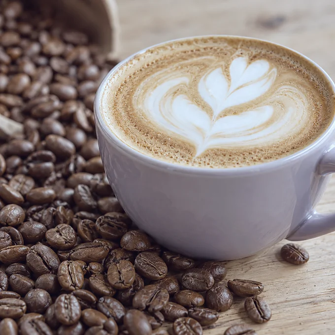 Secangkir cappuccino di antara biji kopi di meja kayu